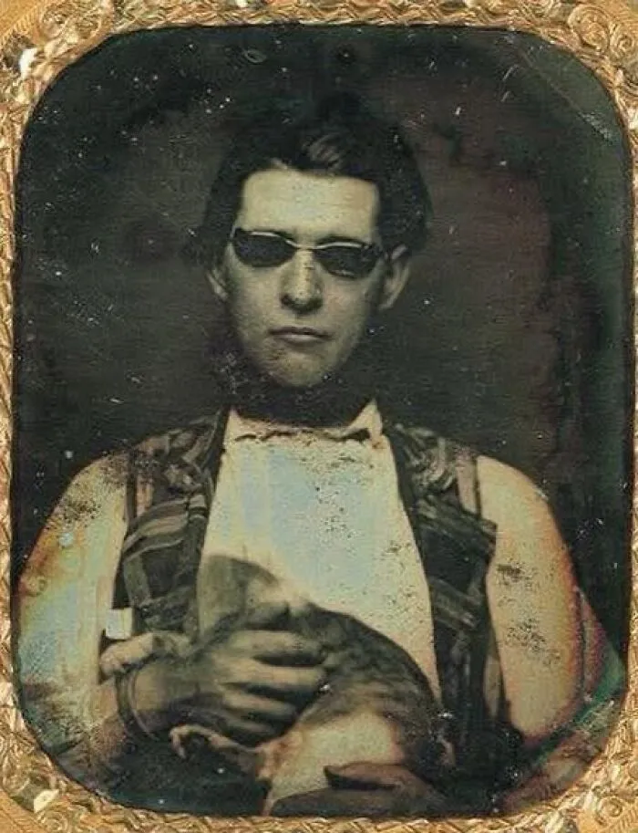 Young man wearing sunglasses in a vintage historical photo, holding a cat, showcasing fascinating moments from the past.