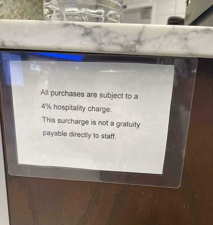 Sign on counter stating a 4% hospitality charge surcharge not payable as gratuity, an example of ridiculous fees.