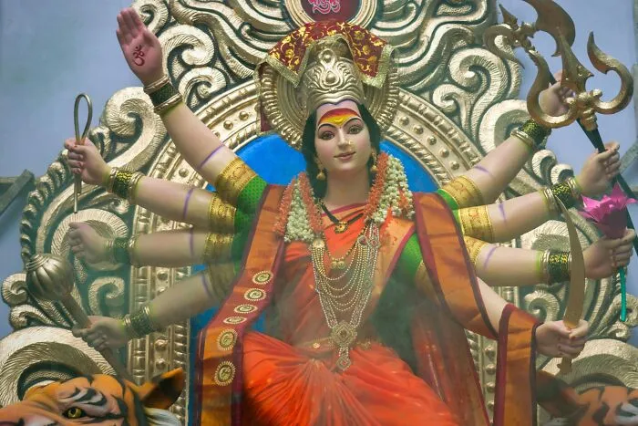 Statue of a multi-armed goddess in a vibrant orange and green outfit symbolizing religious myths and beliefs.