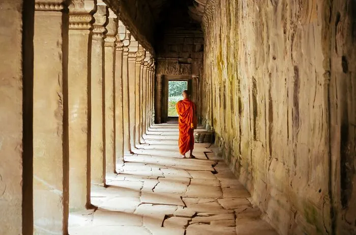 A monk in orange robes walking in an ancient stone corridor symbolic of religious myths and biblical history.