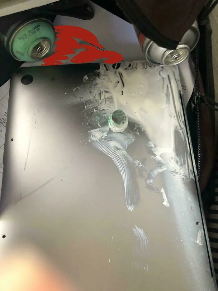 Laptop with spilled white liquid and scattered cans inside a bag, showcasing a funny unfortunate situation from forgetting something.