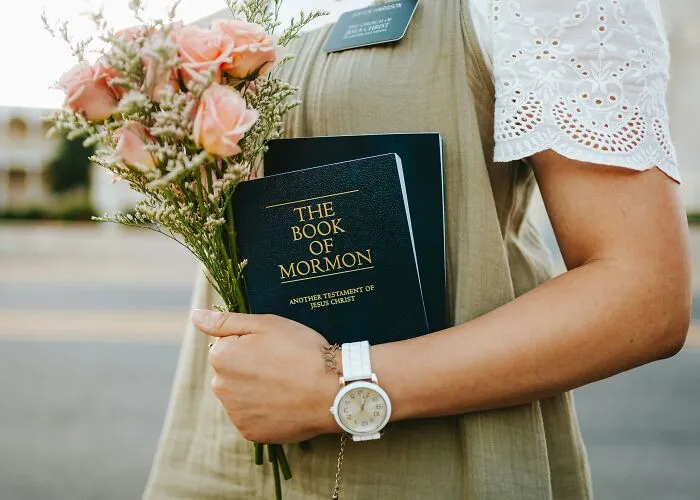 Person holding the Book of Mormon and a bouquet of pink roses, relating to Jesus and religious myths discussion.
