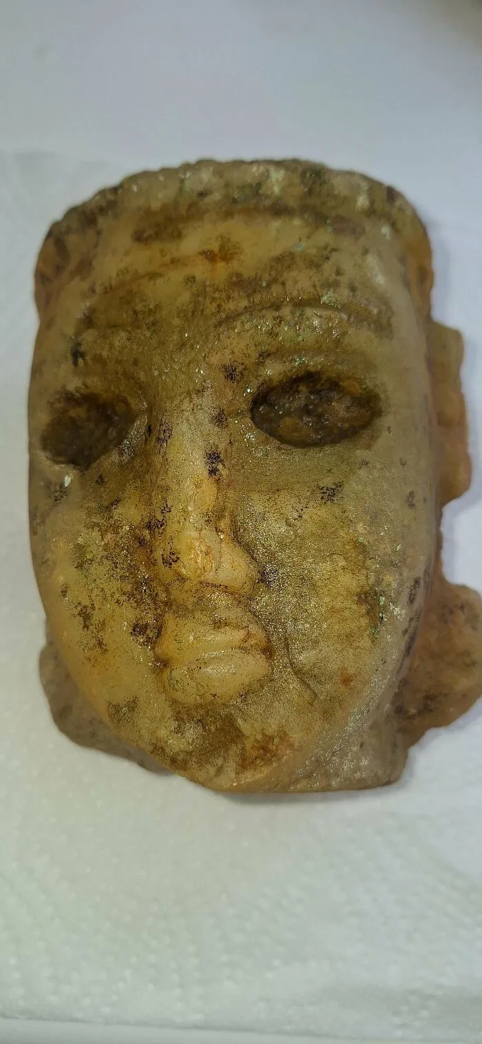Close-up of a weathered old carved stone face, showcasing an interesting and beautiful antique artifact.