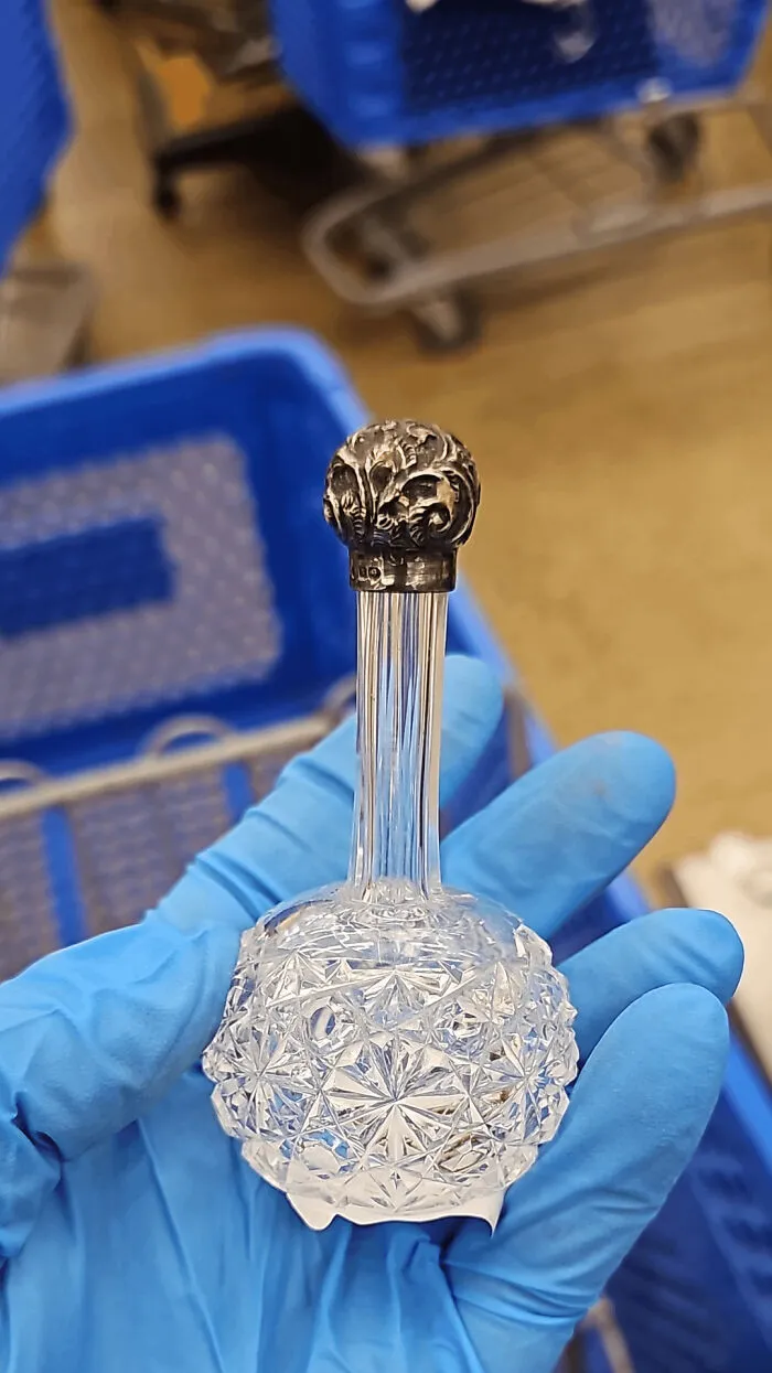 Hand holding a vintage cut glass bottle with an ornate metal stopper, showcasing beautiful old collectible items.