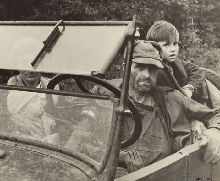 Man and children in a worn car during the Great Depression, showing the hardships faced by families in the past.