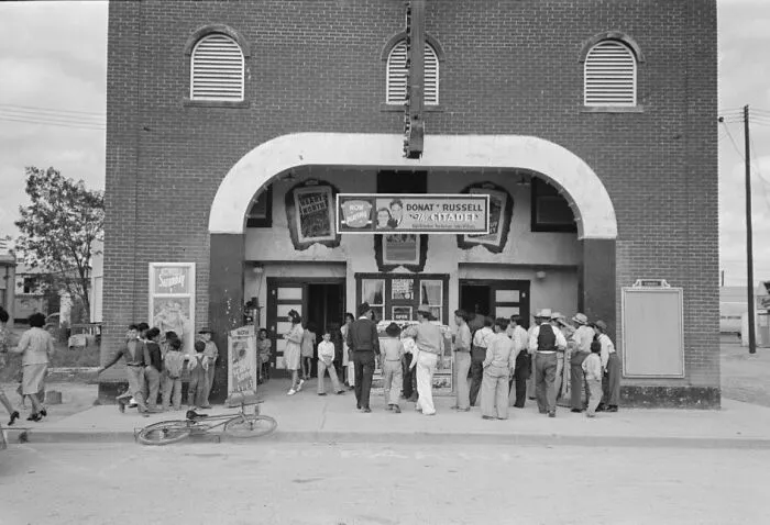 Group of people gathered outside a brick building during the Great Depression era in a black and white photo.