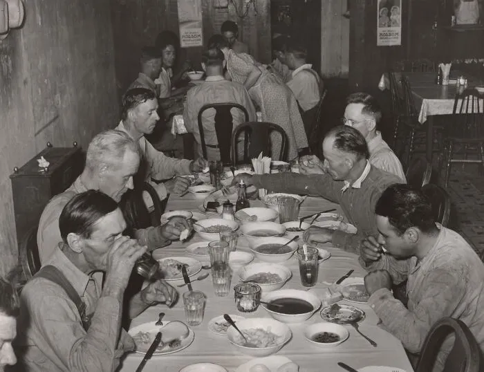 Men eating a meal together at a crowded table in a soup kitchen during the Great Depression era.