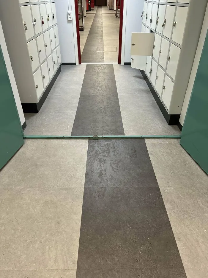 School hallway with rows of lockers on both sides and a mismatched floor pattern in an educational building.