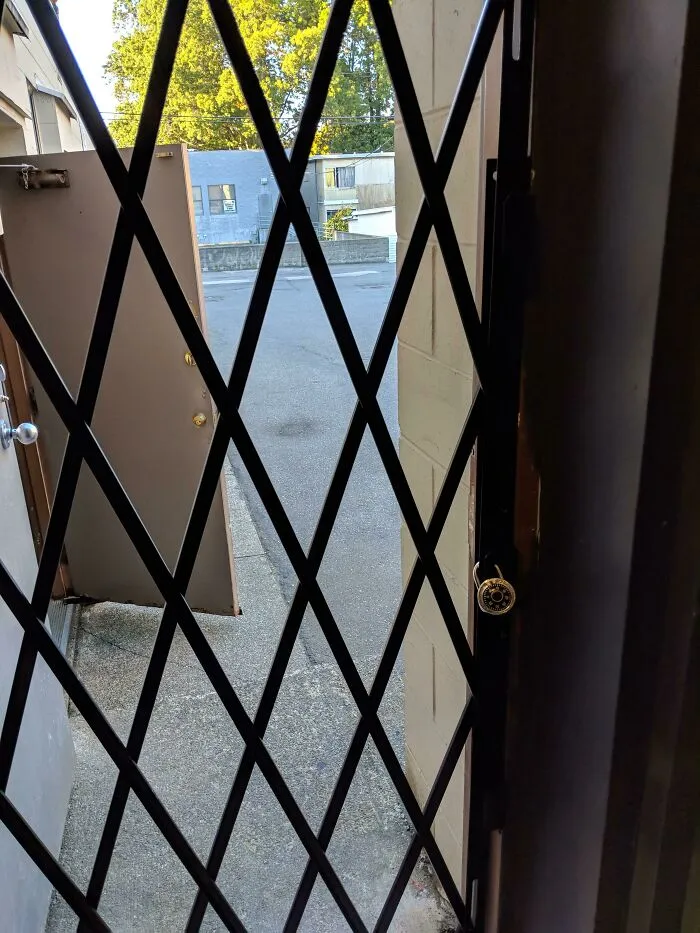 Security gate with a combination lock and an open door showing the outside concrete pathway in a school setting.