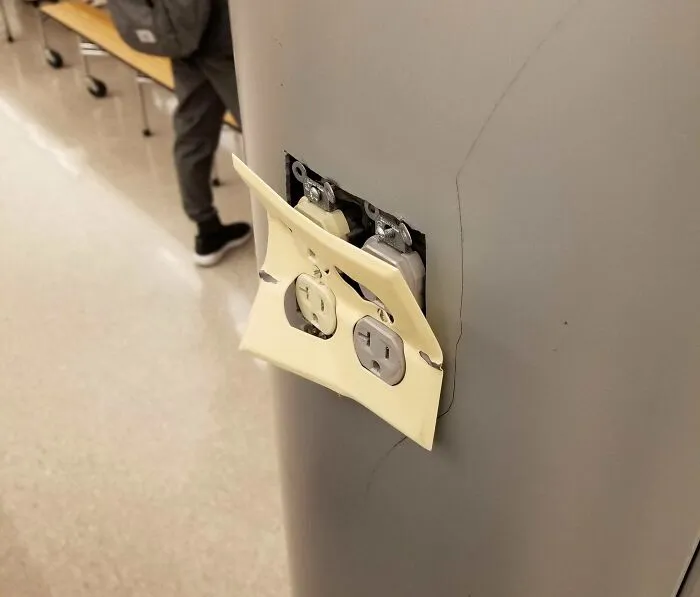 Damaged electrical outlet with cracked cover on a wall inside a school, highlighting unsafe and unequal school conditions.