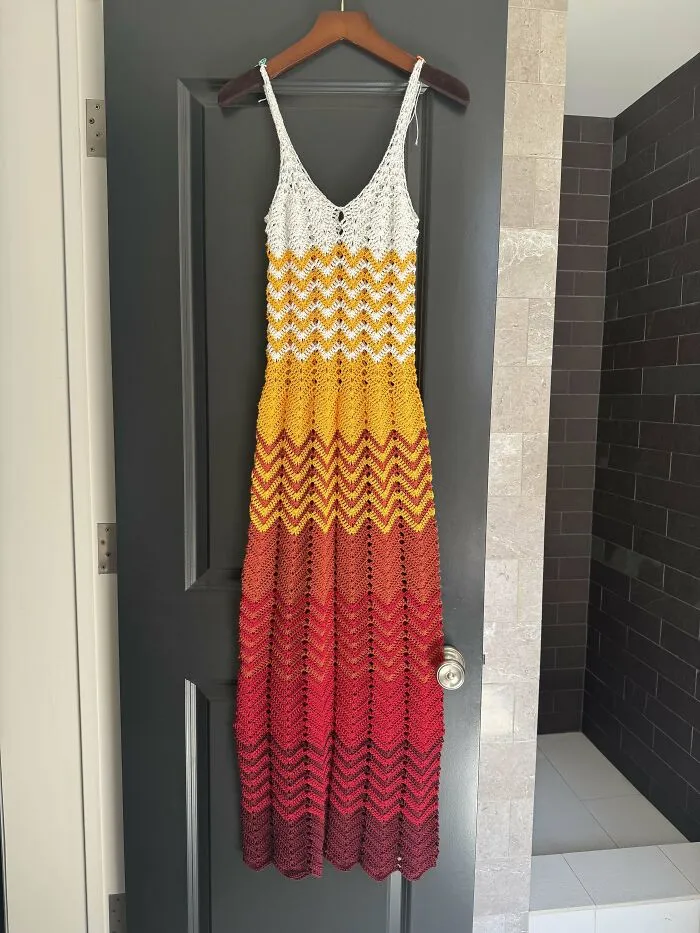 Crochet dress with gradient chevron pattern in white, yellow, orange, red, and brown hanging on a door.