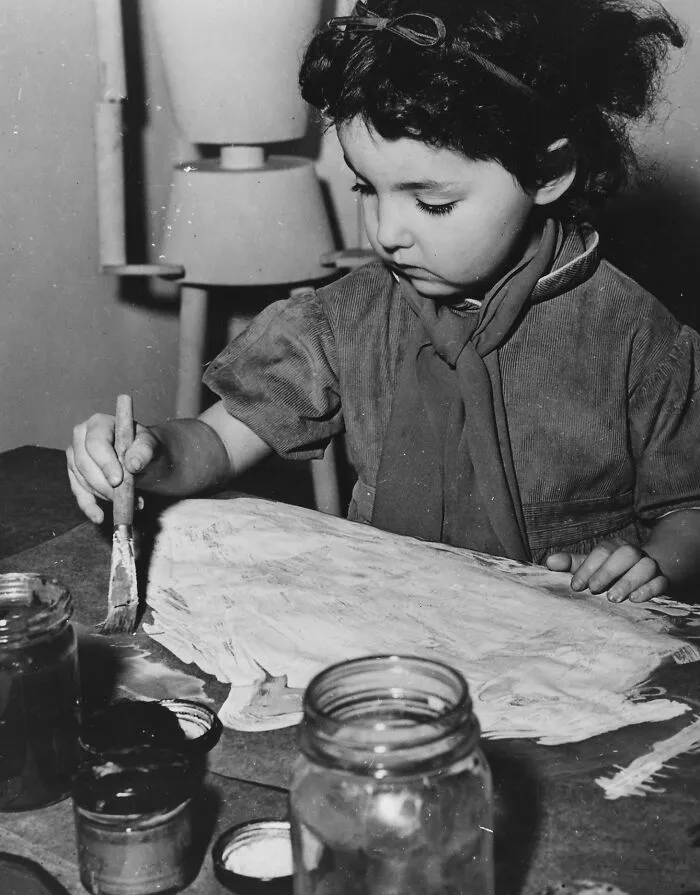 Young girl painting at school desk, showcasing schools worldwide during World War II with art supplies and focused expression.
