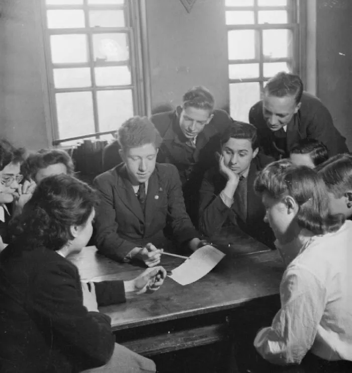 Group of students gathered around a table studying together in a school classroom during World War II.