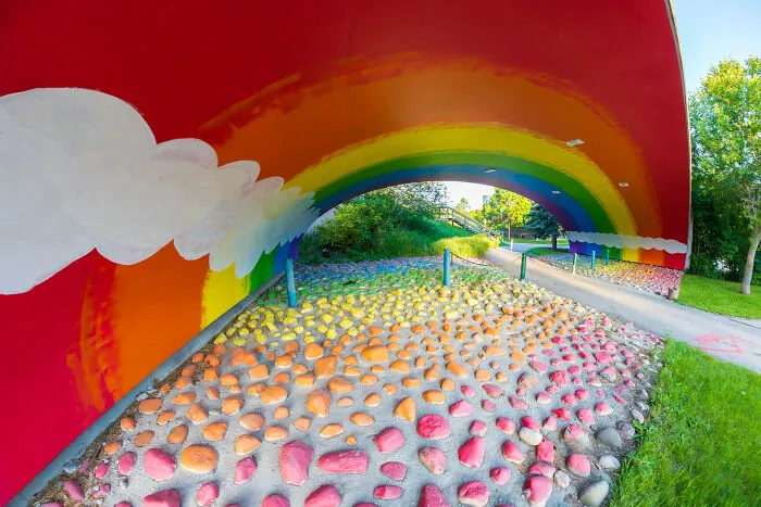 Colorful rainbow mural under a bridge with painted stones on the ground, capturing a modern life boring dystopia scene.