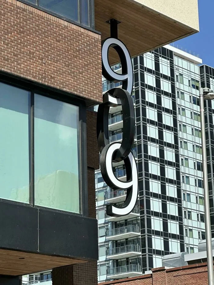 Street view of modern building with creative hanging sign featuring linked numbers 9, showcasing smart design innovation.