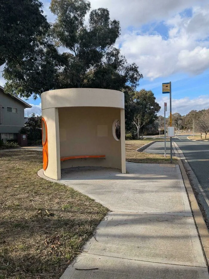 Modern bus stop shelter with circular design and orange bench, showcasing smart and cool design innovation.