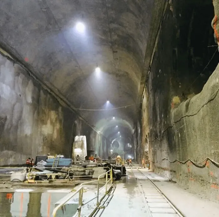 An extremely large and eerie construction tunnel with workers, equipment, and rail tracks, highlighting the scary scale.