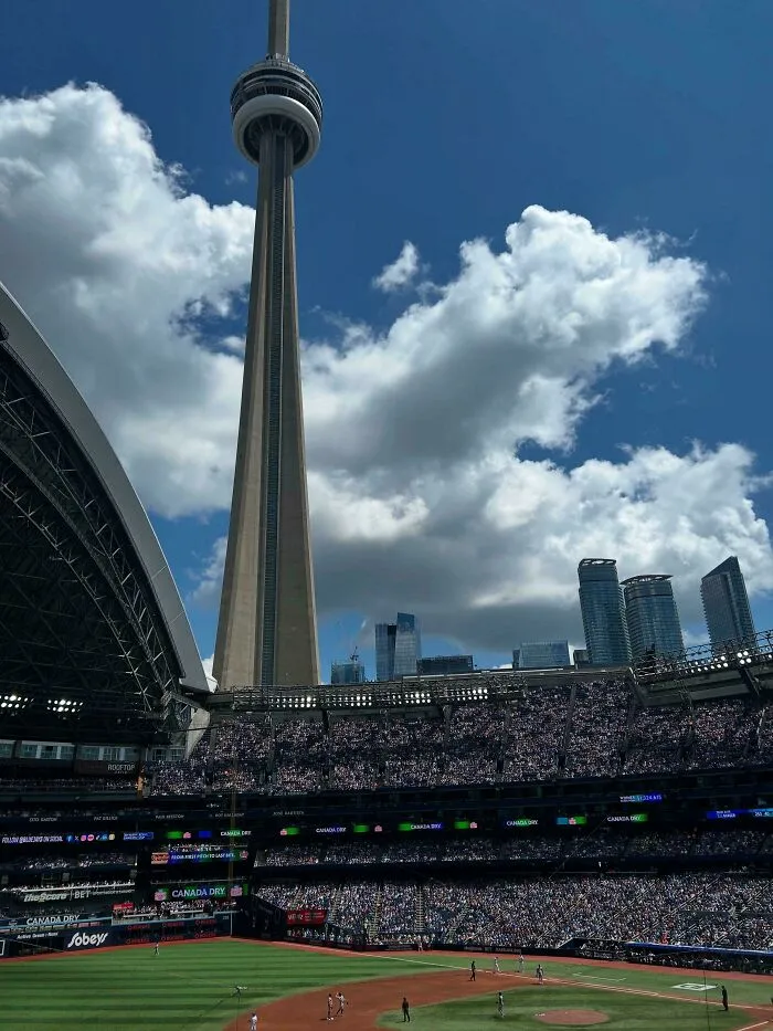 The CN Tower overlooking a filled baseball stadium, an extremely large structure creating a scary and eerie urban landscape.