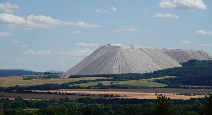 An extremely large salt mountain towering over a vast landscape of fields and forests, showcasing eerie scale.