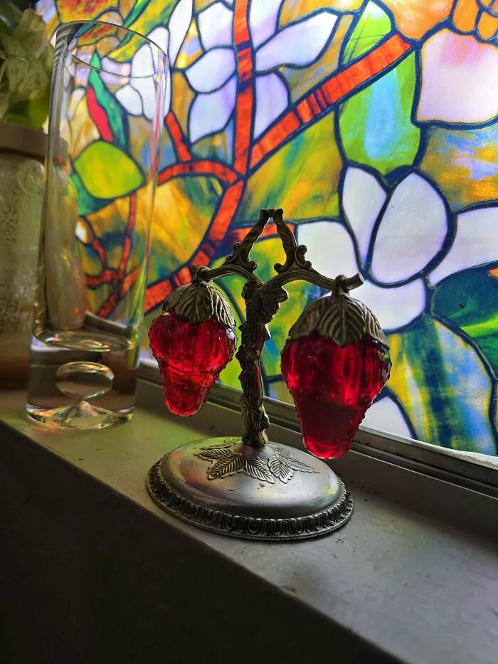 Vintage strawberry-shaped earrings displayed on a silver stand by a colorful stained glass window thrift store finds.