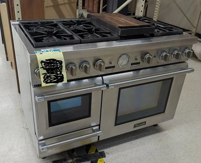 Stainless steel gas range stove with dual ovens and wooden cutting board on top, a rare thrift store find.