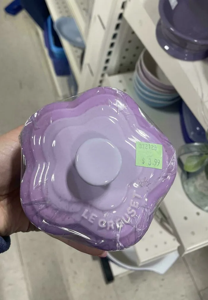 Lavender Le Creuset casserole dish thrift store find priced at 3.99 held in hand with shelves in background.