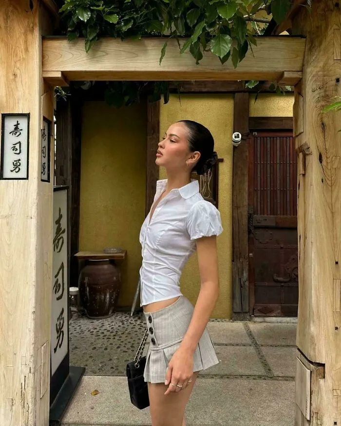 Mujer con blusa blanca y falda gris posa bajo estructura de madera en ambiente exterior, momentos en los que Instagram colapsó.