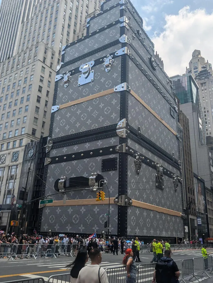 Edificio gigante con diseño de maleta de lujo en ciudad con multitud y barricadas en la calle, cosas interesantes compartidas.
