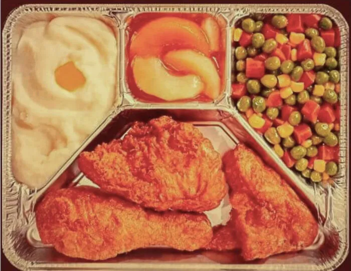 Vintage TV dinner with fried chicken, mashed potatoes, mixed vegetables, and canned peaches evoking nostalgic memories of old age.