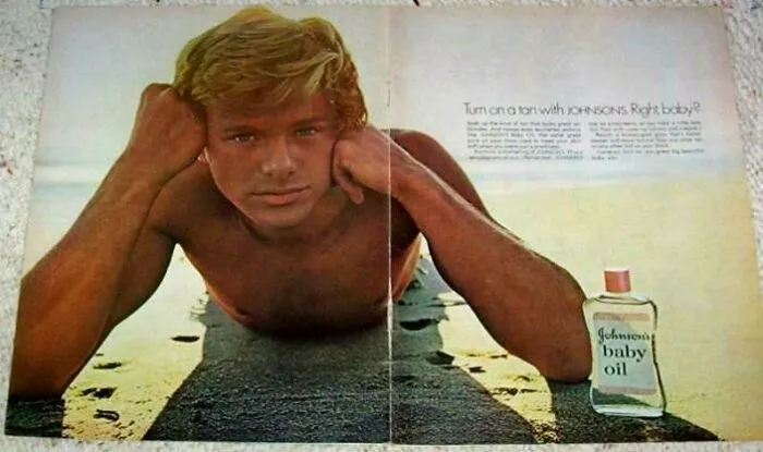 Young man lying on beach sand applying Johnson’s baby oil, evoking nostalgia and memories of old age reflections.