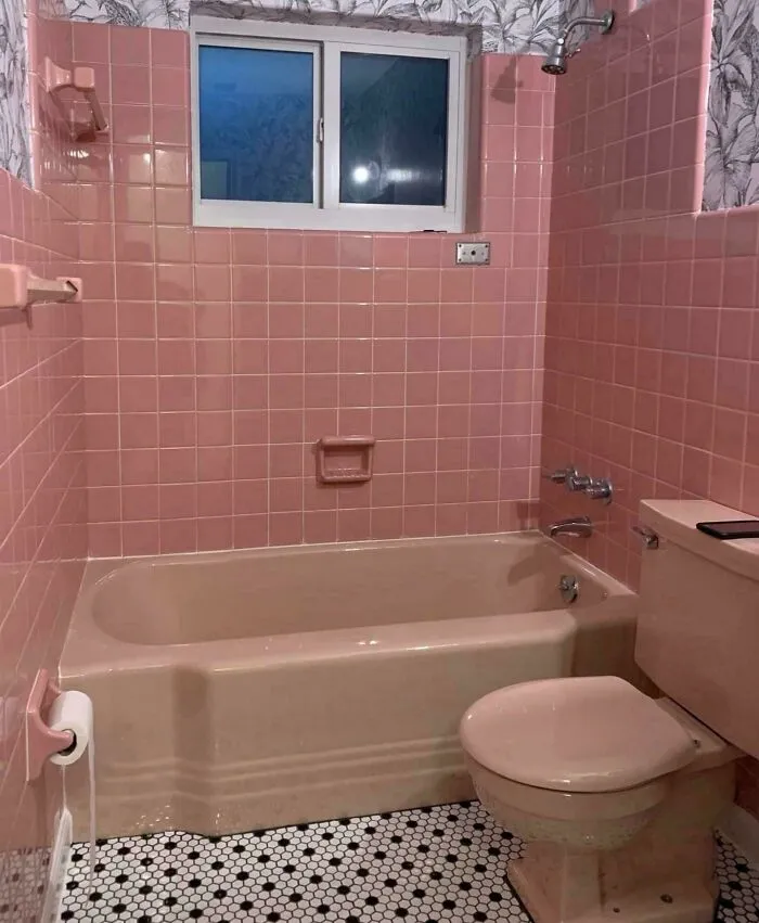 Vintage pink tiled bathroom with bathtub and toilet, evoking nostalgic memories and feelings of old age.