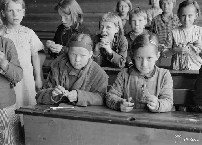 Group of children in school classroom worldwide during World War II, engaged in crafting activities and seated at wooden desks.