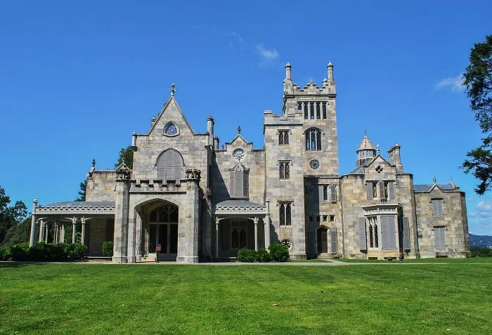 Historic home with Gothic architectural features and stone facade under a clear blue sky in a spacious green lawn setting.