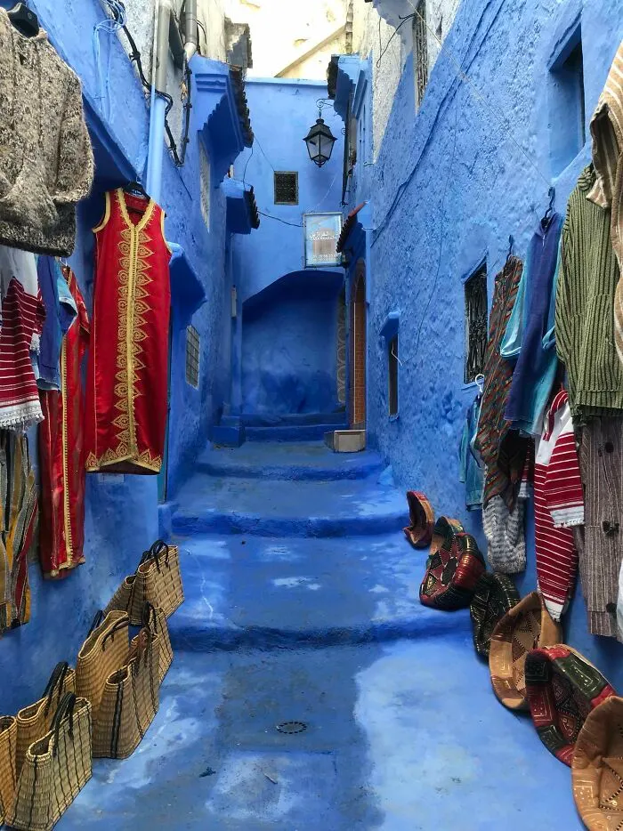 Calle estrecha pintada de azul con ropa y artesanías tradicionales, mostrando detalles ingeniosos en la vida cotidiana.