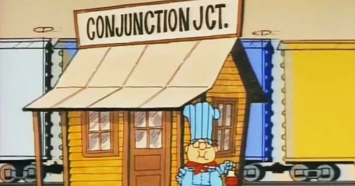 Cartoon scene showing a small wooden train station named Conjunction Jct with a character in a blue chef outfit.