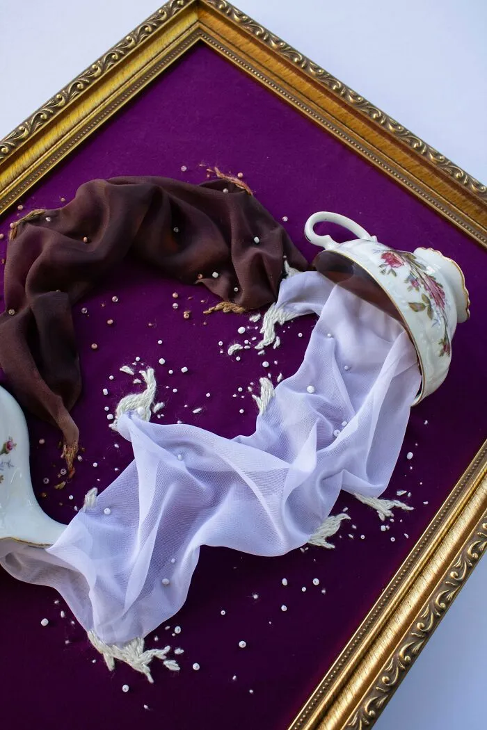 Creative embroidery art featuring white and brown fabric flowing from a floral teacup on a purple background