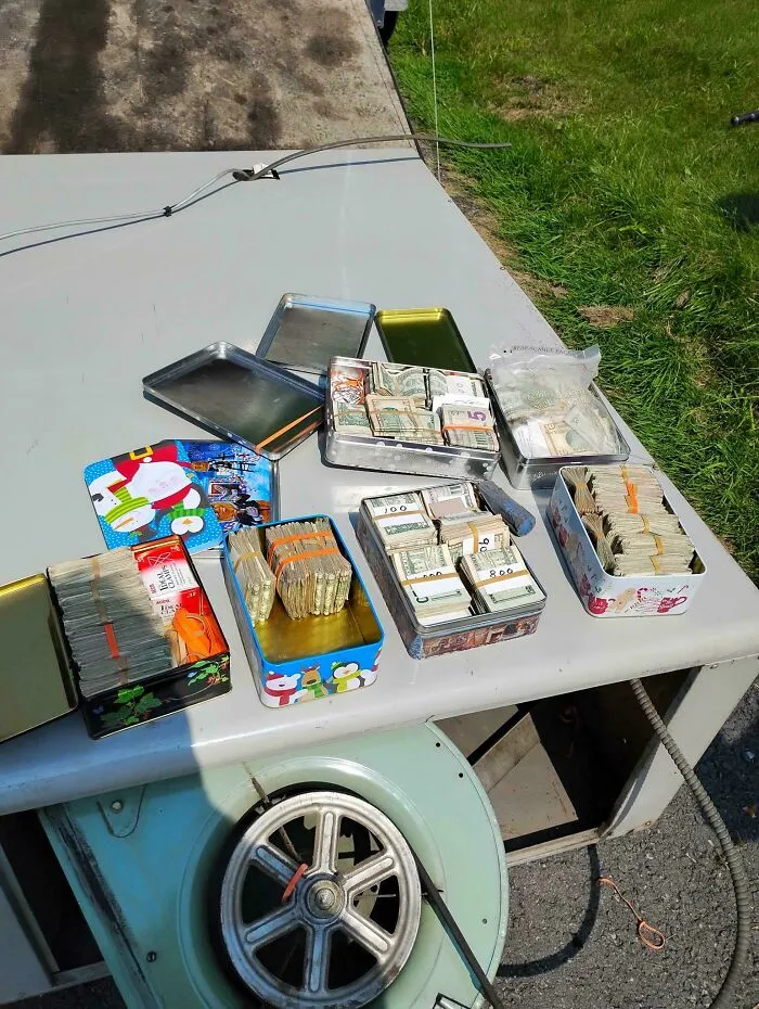 Several tins filled with neatly stacked and bundled cash displayed on a metal surface outdoors, moderately interesting.