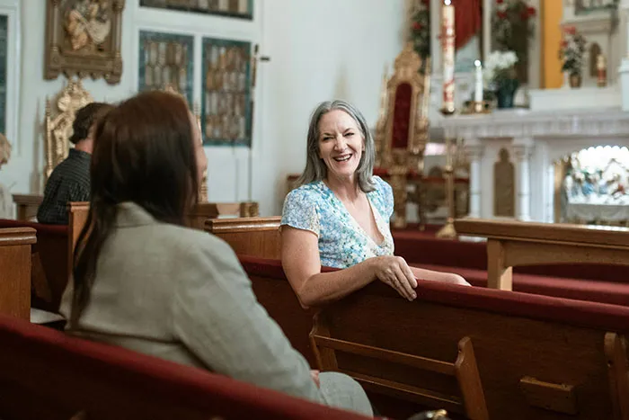 Two women chatting and smiling while seated in wooden pews inside a church discussing microfeminisms and social views.