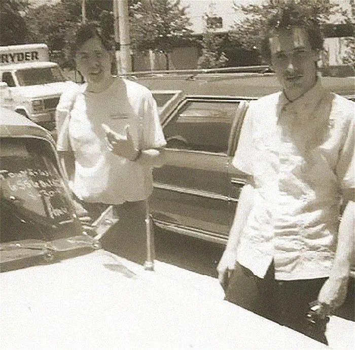 Two people standing next to a car in a vintage black and white photo with a terrifying and horrific backstory.