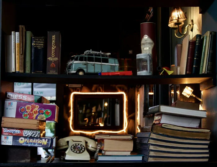 Estantería con libros antiguos, juegos de mesa retro y teléfono clásico, representando tendencias hogareñas de la vieja escuela.
