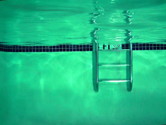 Underwater view of a pool ladder with clear green water, illustrating a rare phobia scenario involving swimming pools.