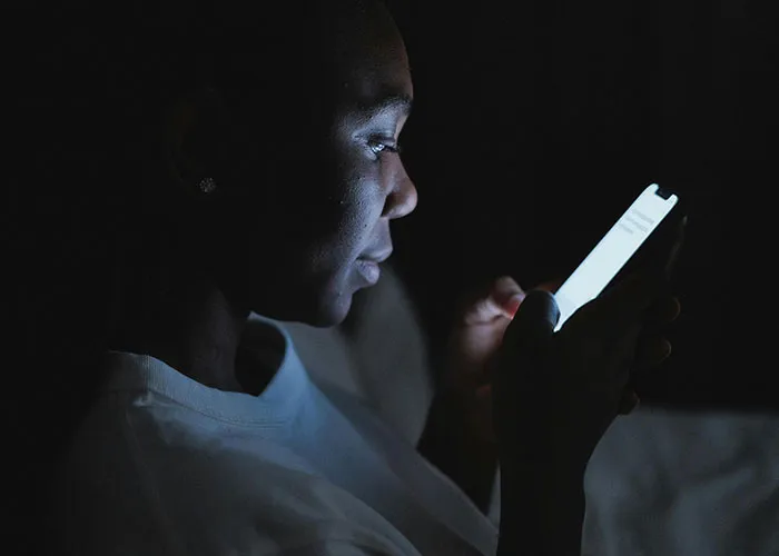 Person reading a glowing phone screen in the dark, illustrating themes related to cheating stories and secrets.