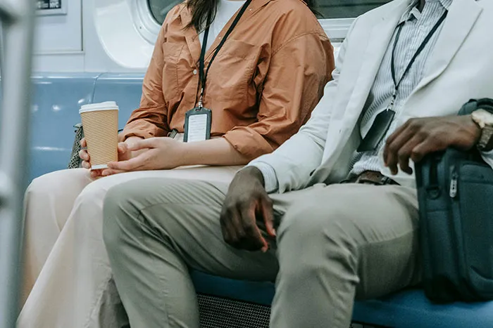 Two commuters sitting on a subway bench, one holding a coffee cup, illustrating diverse urban interactions.