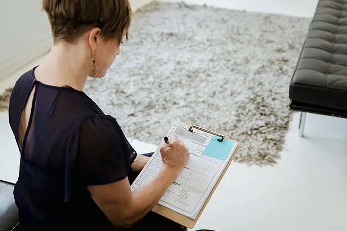 Woman sitting on a chair filling out a form on a clipboard, illustrating microfeminisms discussion on big burly men.
