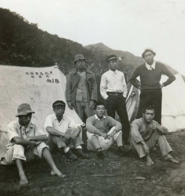 Group of men posing outside tents at a temporary school site during World War II, showcasing schools worldwide history.