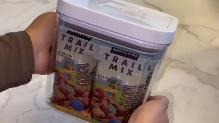 Hands holding a container filled with multiple packs of trail mix, illustrating trends leading to overconsumption.