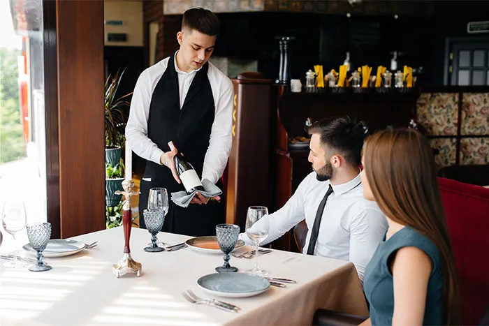 Camarero sirviendo vino a pareja en restaurante mientras observan su servicio durante una cita terrible.