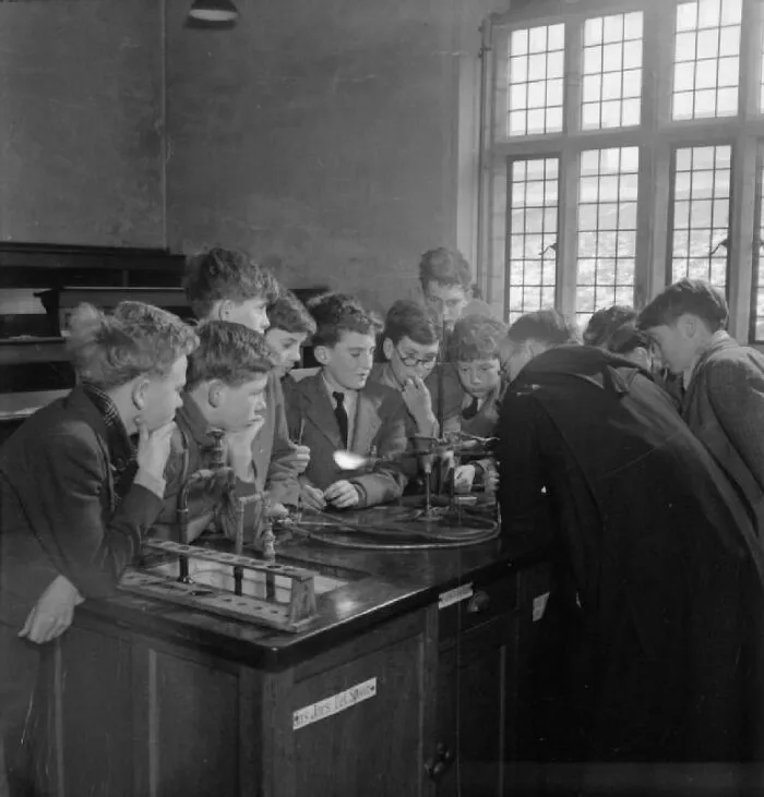 Boys gathered around a science experiment in a school classroom during World War II, demonstrating wartime education.