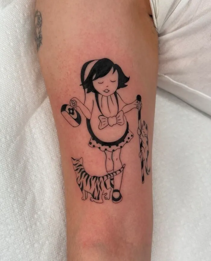 Black ink tattoo of a girl holding a hat and a stick with two cats beside her on a person's arm, best tattoos design.