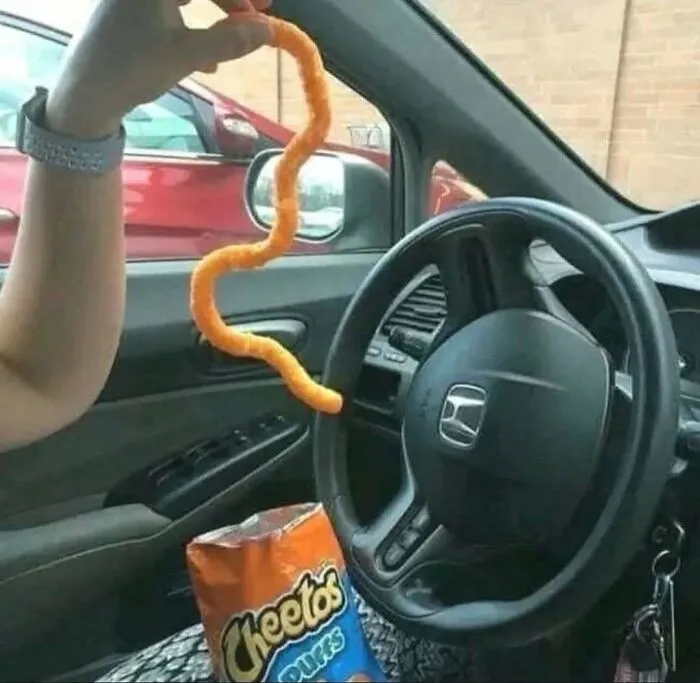 Hand holding an unusually long, wavy Cheetos snack inside a car, a funny and strange picture from no sense photos.